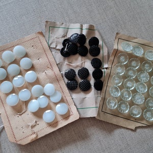 Puede incluir: Tres tarjetas de botones. Una tarjeta tiene 20 botones blancos, otra tiene 10 botones negros y la última tiene 25 botones transparentes con un diseño de flores.