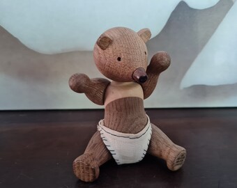 Puede incluir: Un juguete de oso de madera que lleva un pañal blanco. El oso tiene un cuerpo marrón y una cabeza marrón claro con una pequeña nariz negra.