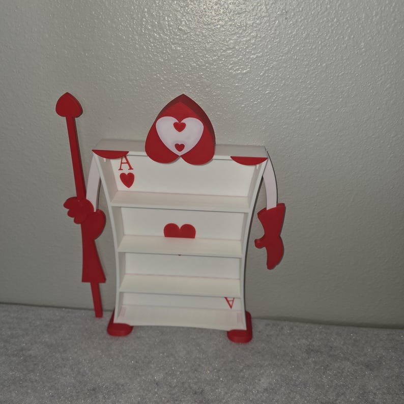 May include: A whimsical, white and red shelf unit shaped like the Queen of Hearts from Alice in Wonderland. The unit has three shelves, red heart accents, and a red scepter. The card suit symbols are visible on the shelf.