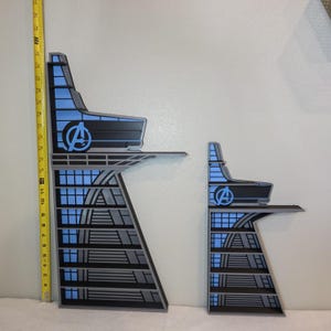 May include: Two-piece set of stylized building cutouts, featuring a blue and black color scheme with the Avengers logo. The larger piece measures approximately 12 inches tall. The design includes geometric shapes and a modern aesthetic.
