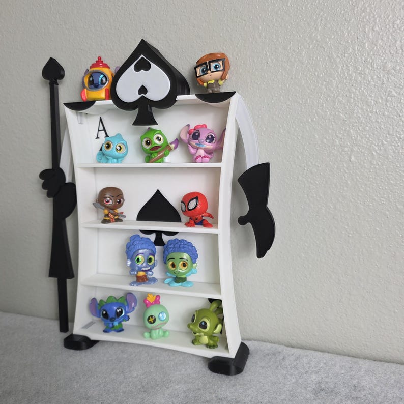 May include: A white Ace of Spades-shaped shelf unit with multiple shelves, displaying various colorful character figurines. The shelf has a black spade design and a black base. The figurines include characters from popular animated movies and comics.