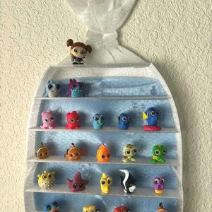 May include: A clear plastic display case filled with colorful figurines of characters from the animated film "Finding Nemo." The case has multiple shelves and is mounted on a textured wall. The figurines are various sizes and shapes.
