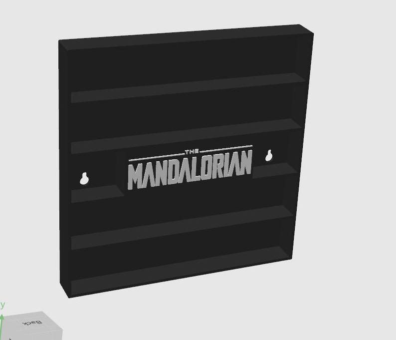 May include: A black wall-mounted display shelf featuring four horizontal tiers for storage. The center of the unit displays the silver-colored text THE MANDALORIAN in a bold, stylized font. Two keyhole-shaped mounting slots are visible on the back panel.