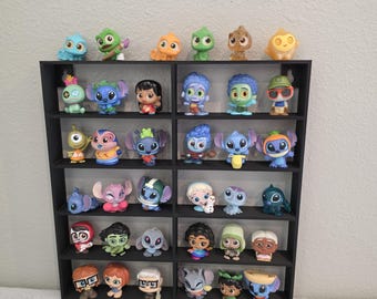 May include: A black display unit holding a collection of colourful character figurines. The figurines, of varying sizes and designs, depict characters from popular animated films. The unit is set against a plain white wall, highlighting the collection.