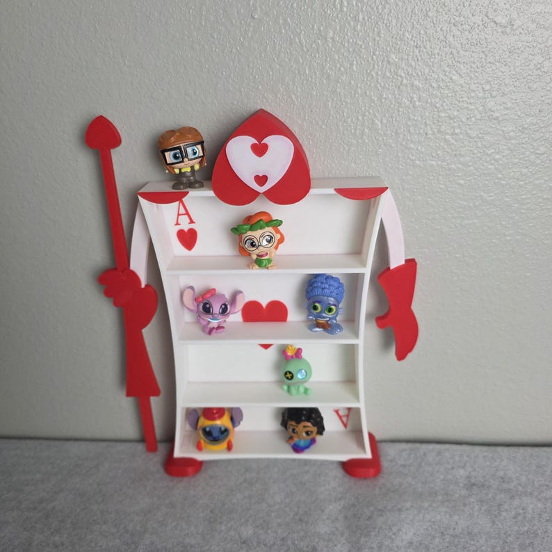 May include: A white, heart-shaped shelf unit with red accents, resembling an Ace of Hearts playing card. The shelf holds several small character figurines. The unit has a red spear on the left side and red arms and feet.