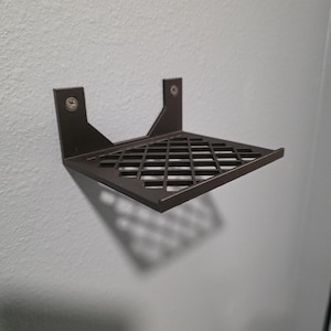 Puede incluir: Una estantería de pared de metal marrón oscuro con un patrón de diamantes en la superficie de la estantería. La estantería está montada en una pared gris claro con dos tornillos. La estantería está diseñada para guardar objetos pequeños.