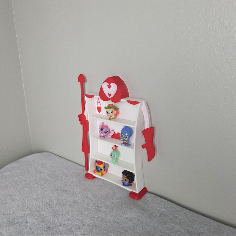May include: A whimsical, red and white shelf shaped like the Ace of Hearts card. The shelf has multiple levels holding small character figurines. The top of the shelf features a heart design and the letter "A".