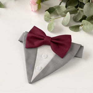 Puede incluir: Un pa&ntilde;uelo triangular para mascotas con dise&ntilde;o de esmoquin, que presenta una tela exterior gris, un panel central blanco con dos botones peque&ntilde;os blancos y una pajarita de color burdeos oscuro unida al borde superior.