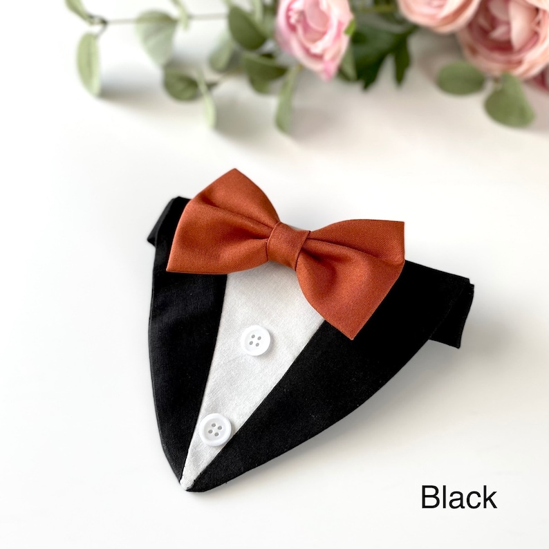 May include: A black and white tuxedo-style pet bandana featuring a rust-colored fabric bow tie attached at the top. The front panel is white with two small white buttons sewn vertically down the center, framed by black fabric sides. The word Black is printed in the bottom right corner.