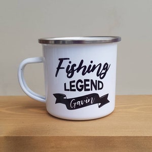 May include: A white enamel mug with a silver rim and a handle. The mug features black text that reads Fishing LEGEND with the name Gavin printed in white script inside a black banner graphic centered on the front of the mug.