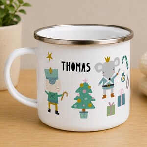May include: A white enamel mug with a silver rim featuring a colorful Christmas-themed illustration of a nutcracker, a mouse wearing a crown, a decorated pine tree, gifts, and the name THOMAS printed in black capital letters on the front.