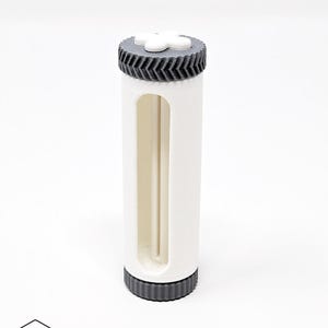May include: A white cylindrical container with a rectangular cutout, topped and bottomed with dark gray, ridged caps. The top cap features a white, four-petal design. The container is labeled with the text "NTH FORM" and a logo.