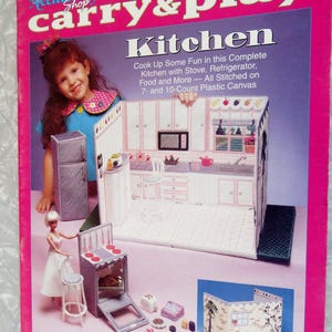 May include: A pink and purple box set for a doll kitchen, featuring a miniature kitchen scene with a stove, refrigerator, and accessories. The text on the box reads "Plastic Canvas Fashion Doll Carry & Play Kitchen."
