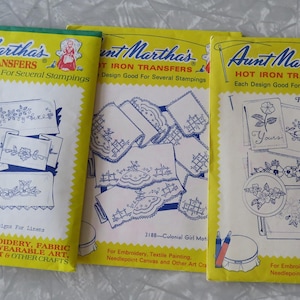 May include: Three vintage Aunt Martha's Hot Iron Transfer packets. The packets are yellow with blue and white designs, featuring floral and colonial motifs. Text includes "Flowers for Linens" and "Charming Designs for Linens". Each design is good for several stampings.
