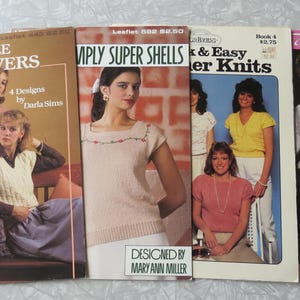 May include: Four knitting pattern leaflets featuring different designs. The first leaflet is titled "Cable Pullovers" and features a woman wearing a pink cable knit sweater. The second leaflet is titled "Simply Super Shells" and features a woman wearing a white shell stitch sweater. The third leaflet is titled "Quick & Easy Summer Knits" and features three women wearing different summer knit sweaters. The fourth leaflet is titled "Fashion" and features a woman wearing a white lace sweater.