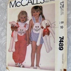 May include: A vintage McCall's sewing pattern for a toddler size bunny costume. The pattern is for a bunny outfit with a white and blue polka dot fabric and a white bunny head with pink ears. The pattern number is 7489.