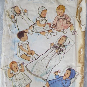 May include: A vintage Simplicity 6072 sewing pattern envelope for newborn clothing. The front features illustrations of infants wearing various gowns, dresses, and bonnets in white, pink, and blue. The paper envelope shows significant wear and staining.
