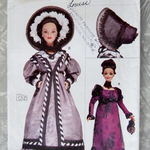 May include: Vogue Craft sewing pattern 7296 featuring doll clothing designs. The pattern includes a doll wearing a long, lavender dress with black and white trim, and a large hat. Another doll is wearing a long, purple dress with black lace.