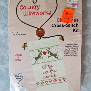 May include: A Country Wireworks Christmas cross-stitch kit. The kit includes a black wire heart-shaped towel bar with a wood bead, Aida cloth, needle, floss, and instructions. The design features reindeer and the words "Joy to the World."