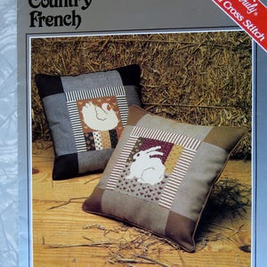 May include: A cross stitch pattern booklet featuring two pillow designs. The pillows are made with a patchwork of fabrics in brown, white, and red. The pillows feature a white chicken and a white rabbit. The booklet cover reads "Country French" and "Yours Truly Counted Cross Stitch".