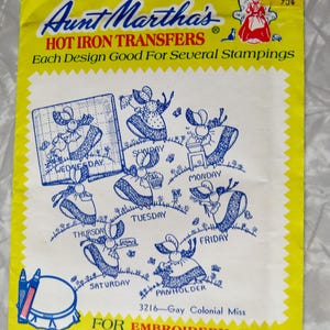 May include: Aunt Martha's Hot Iron Transfers package, predominantly yellow with a red border. It features blue illustrations of a colonial woman engaged in daily tasks, each labelled with a day of the week. Text includes "For Embroidery, Fabric Painting..."