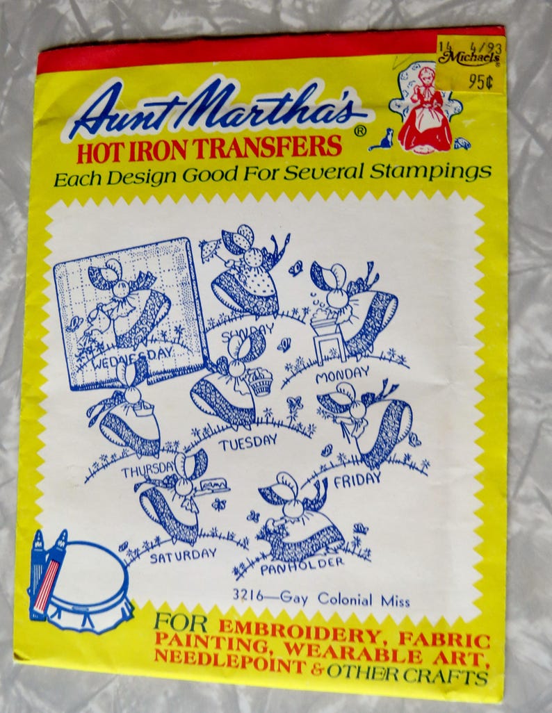 May include: Aunt Martha's Hot Iron Transfers package, predominantly yellow with a red border. It features blue illustrations of a colonial woman engaged in daily tasks, each labelled with a day of the week. Text includes "For Embroidery, Fabric Painting..."