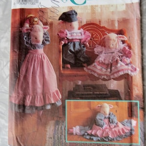 May include: Simplicity Crafts sewing pattern featuring doll designs. The cover shows three dolls in pink and blue outfits, with one doll in a dress and two dolls in pants. The pattern is by Faith Van Zanten.