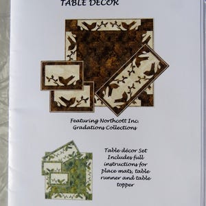 May include: A printed page with the title "WARBLERS TABLE DECOR" and the text "Featuring Northcott Inc. Gradations Collections." The image shows table decor designs with bird and branch motifs, including place mats, a table runner, and a table topper.