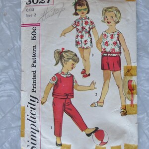 May include: Vintage Simplicity pattern envelope featuring illustrations of children's clothing. The cover displays a child's size 2 pattern with drawings of a romper, shorts set, and pants set. The pattern number is 3027.