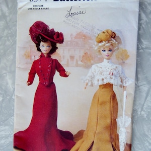 May include: A vintage Butterick sewing pattern featuring two dolls in period clothing. One doll wears a red dress and feathered hat, the other a gold skirt and white lace top. The pattern is labeled "6374" and "Louise."