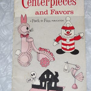 May include: Vintage book cover titled "Centerpieces and Favors" with illustrations of a pink bunny pulling a cart, a clown, a ghost, a house, and a baby carriage. The text "A Pack-o-Fun PUBLICATION" is also visible.
