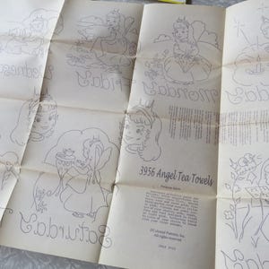 May include: A vintage paper pattern for 3956 Angel Tea Towels, featuring line drawings of angels and days of the week in cursive. The paper is off-white with faded ink, showing signs of age.
