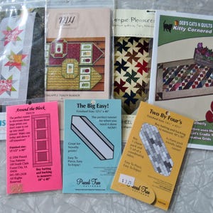 May include: Assortment of quilting patterns, including "Desert Stars," "Pineapple Punch Runner," and "Kitty Cornered." The patterns feature various designs, such as star, pinwheel, and geometric patterns. The "Around the Block" pattern is 15.5" x 44".