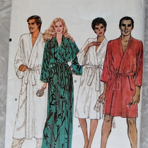 May include: A Very Easy Very Vogue sewing pattern envelope for size X-LARGE. The front features illustrations of four individuals wearing robes: a long white robe, a long teal robe with a black leaf pattern, a short white robe, and a short red robe.