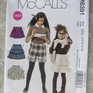 May include: McCall's M6391 sewing pattern featuring illustrations of children's clothing, including shorts and a tiered skirt. The pattern includes the size range CHJ (7-8-10-12-14). The word "EASY" is in a pink circle.
