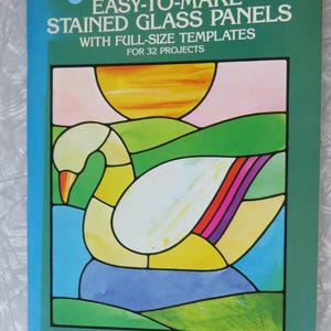 May include: A softcover book titled Ed Sibbett, Jr. Easy-to-Make Stained Glass Panels with Full-Size Templates for 32 Projects. The cover features a colorful stained glass illustration of a swan on water with a yellow sun and green hills.