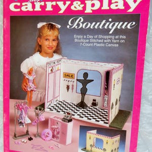 May include: A pink plastic canvas kit for a fashion doll boutique. The cover features a young girl and a completed boutique model with dressing rooms, a sale sign, and a cash register. The text reads "Fashion Doll Carry & Play Boutique."