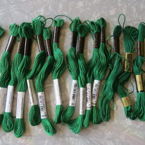 May include: A collection of fourteen skeins of green embroidery floss arranged in a row. Each skein features a paper label with a barcode and the number 6228, along with the brand name J. & P. Coats printed on the gold-colored paper bands.