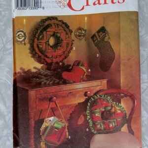 May include: Simplicity Crafts pattern 8159 featuring holiday decor projects including a wreath, stockings, a heart-shaped pillow, and a small bag. The envelope displays images of these items in red, green, and plaid fabrics with gold accents.