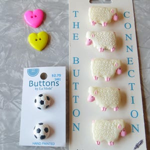 May include: A package of white sheep button covers with pink accents. The package says "Designer Button Covers" and "Connection Button". There are also two pink heart buttons, two yellow heart buttons, and two black and white soccer ball buttons.