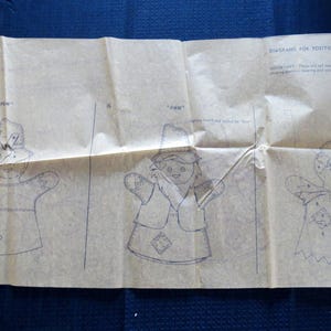 May include: A vintage sewing pattern, featuring three hand-drawn illustrations of a puppet design. The diagrams show the puppet's body, hat, and clothing, with the word "PAW" and "MAW" written above the drawings. The pattern is on aged, tan paper.