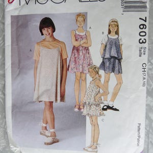 May include: A sewing pattern for girls' dresses. The pattern includes three different styles: a sleeveless dress with a floral print, a sleeveless dress with a polka dot print, and a dress with a short-sleeved top and a skirt. The pattern is for sizes 7, 8, 10.
