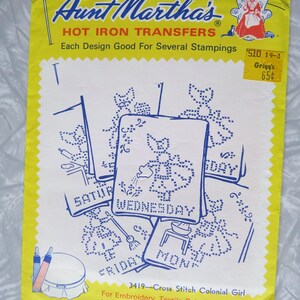 May include: A vintage Aunt Martha's Hot Iron Transfers package. The yellow and white package features blue cross-stitch designs for each day of the week. Includes the text "Cross Stitch Colonial Girl" and a price tag.