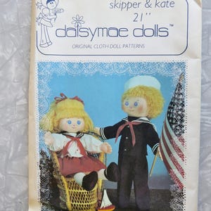 May include: A vintage Daisymae Dolls pattern for making 21-inch Skipper and Kate dolls. The pattern features a color illustration of the dolls dressed in sailor outfits, with Kate sitting in a wicker chair and Skipper holding an American flag.