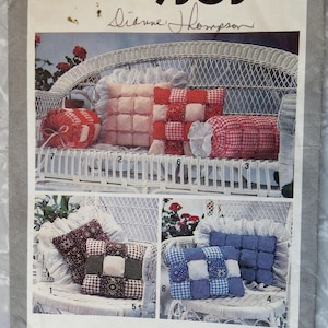 May include: Simplicity 9303 sewing pattern featuring various quilted pillow designs. The image shows several pillows in red, white, and blue fabrics, with a white wicker bench in the background. The pattern includes multiple pillow styles.