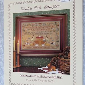 May include: A framed Noah's Ark sampler with a cross-stitch design. The sampler features an alphabet, animals, and the text "And they went in unto Noah into the ark, two and two of all flesh wherein is the breath of life." The artwork is by Margaret Jeffries McKee.