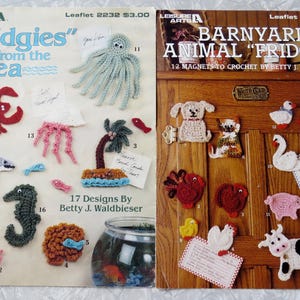 May include: Two vintage crochet pattern leaflets. One features sea creatures like a lobster, octopus, and seahorse. The other showcases barnyard animals, including a dog, cat, and cow. Both are designed to be magnets.