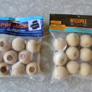 May include: Two clear plastic bags containing unfinished wooden spheres. The left bag is labeled Wood Doll Pin Head, 10 pieces, 0.625 inches. The right bag is labeled Woodpile Fun Wood Ball Knobs, 12 pieces, 1.25 inches. Each sphere has a center hole.