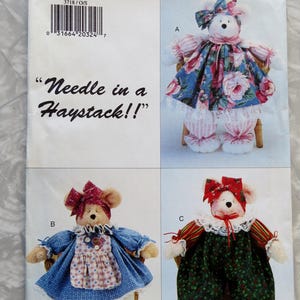 May include: A sewing pattern for making three stuffed animal toys. The pattern is called "Needle in a Haystack!" and includes instructions for making a bear wearing a pink and white dress, a bear wearing a blue and white dress, and a bear wearing a green and white jumpsuit.