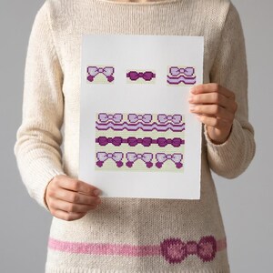 Könnte beinhalten: Ein weißes Blatt Papier mit einem Kreuzstichmuster aus verschiedenen violetten und hellvioletten Schleifen. Das Design umfasst einzelne Schleifenmotive und horizontale Bordürenmuster mit Wellenlinien, alles im pixeligen Rasterstil.